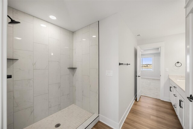 bathroom with wood-type flooring, tiled shower, and vanity