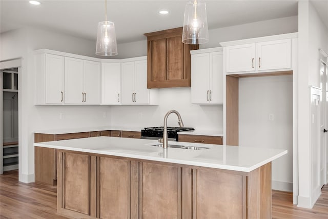 kitchen featuring sink, light hardwood / wood-style flooring, white cabinets, hanging light fixtures, and an island with sink