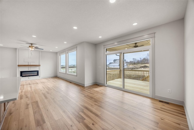 unfurnished living room with ceiling fan, light hardwood / wood-style floors, and a textured ceiling