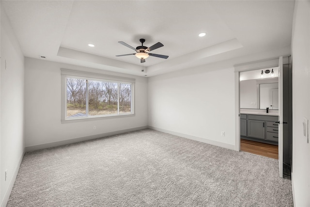 unfurnished bedroom with ceiling fan, a raised ceiling, light colored carpet, and ensuite bathroom