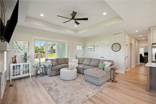 living room featuring ceiling fan, a tray ceiling, and light hardwood / wood-style flooring