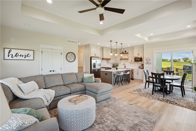 living room with ceiling fan, a tray ceiling, and light wood-type flooring