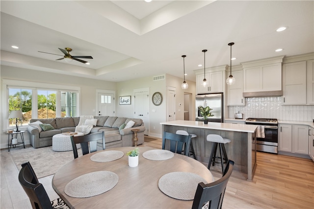 dining room with light hardwood / wood-style flooring, a raised ceiling, and ceiling fan