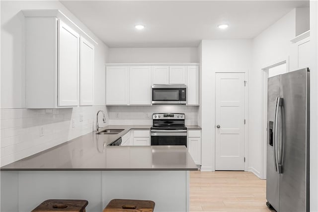 kitchen with white cabinetry, sink, a kitchen bar, kitchen peninsula, and stainless steel appliances