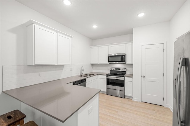 kitchen with sink, appliances with stainless steel finishes, white cabinetry, light hardwood / wood-style floors, and kitchen peninsula