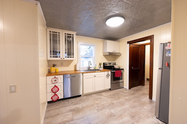 kitchen with sink, appliances with stainless steel finishes, wooden walls, white cabinets, and wood counters