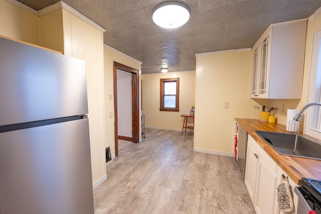 kitchen with sink, butcher block countertops, electric range oven, stainless steel fridge, and white cabinets