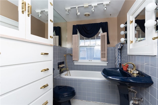 bathroom with tiled bath, toilet, rail lighting, and tile walls