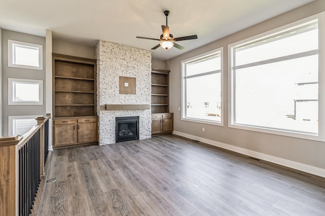 unfurnished living room with built in features, a stone fireplace, light wood-type flooring, and ceiling fan