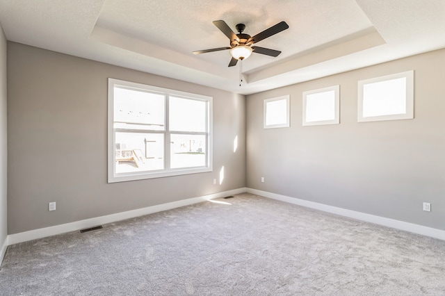 empty room with light carpet, a tray ceiling, and ceiling fan