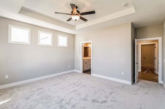 unfurnished bedroom with connected bathroom, carpet floors, a tray ceiling, and ceiling fan