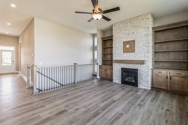 unfurnished living room with light hardwood / wood-style flooring, a stone fireplace, built in shelves, and ceiling fan