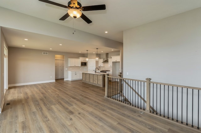 unfurnished living room with hardwood / wood-style floors, sink, and ceiling fan