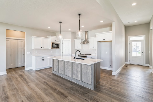 kitchen featuring a center island with sink, wall chimney range hood, built in microwave, and white cabinets