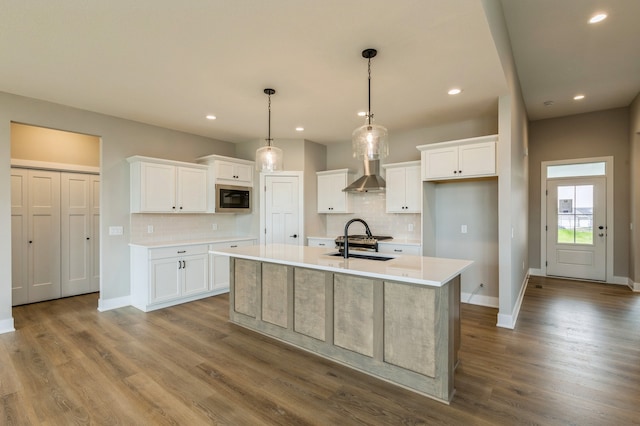 kitchen featuring white cabinets, wall chimney exhaust hood, stainless steel microwave, and a kitchen island with sink