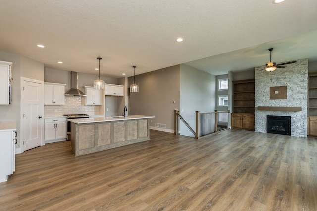 kitchen with wood-type flooring, white cabinetry, wall chimney exhaust hood, stainless steel stove, and a center island with sink