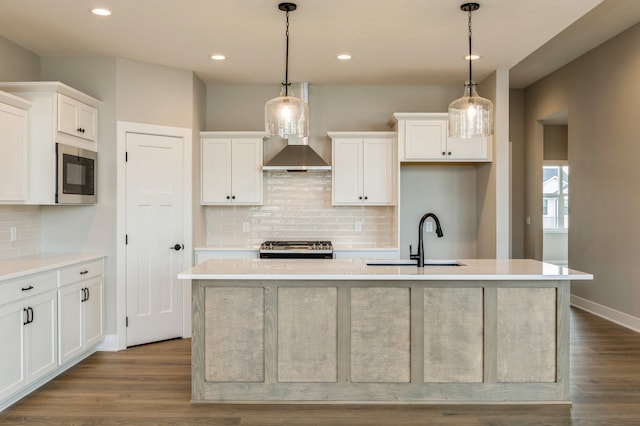 kitchen featuring a kitchen island with sink, hanging light fixtures, stainless steel appliances, sink, and white cabinetry