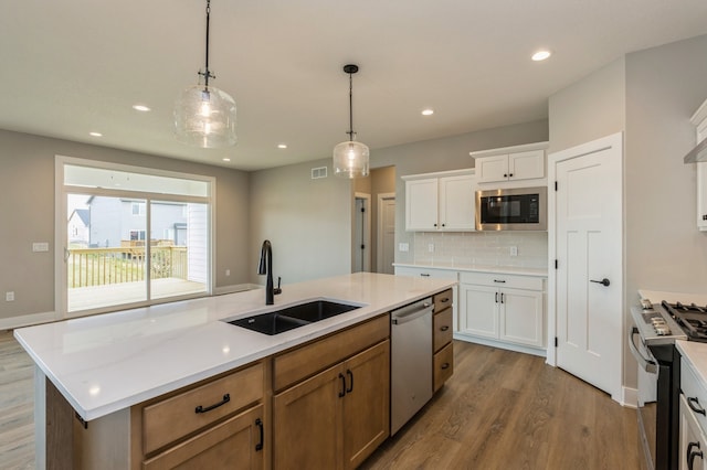 kitchen featuring a kitchen island with sink, stainless steel appliances, wood-type flooring, sink, and white cabinetry