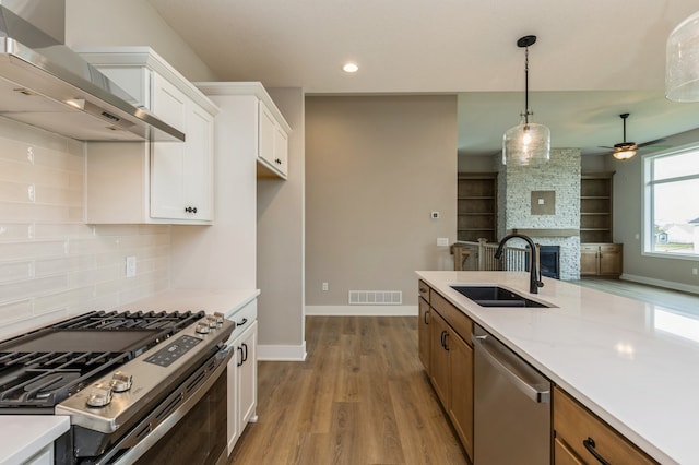 kitchen featuring wall chimney range hood, sink, white cabinetry, stainless steel appliances, and light stone counters