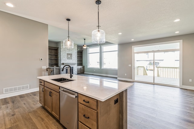 kitchen featuring a center island with sink, dishwasher, a fireplace, pendant lighting, and sink