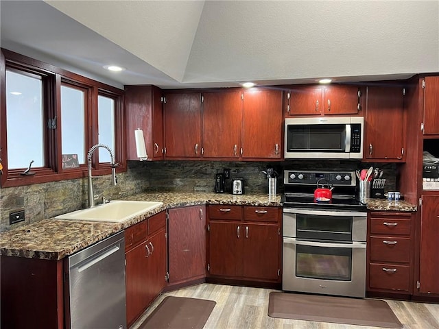 kitchen with appliances with stainless steel finishes, sink, light wood-type flooring, and decorative backsplash