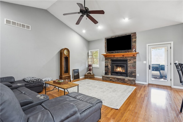 living room featuring a stone fireplace, high vaulted ceiling, ceiling fan, and light wood-type flooring