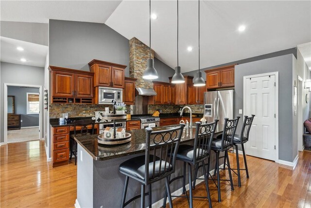 kitchen with a breakfast bar area, light hardwood / wood-style flooring, backsplash, stainless steel appliances, and a center island with sink