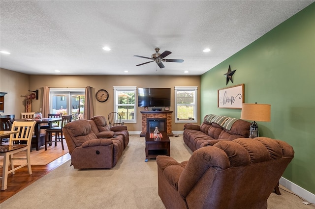 living room featuring wood-type flooring, a textured ceiling, a brick fireplace, and ceiling fan