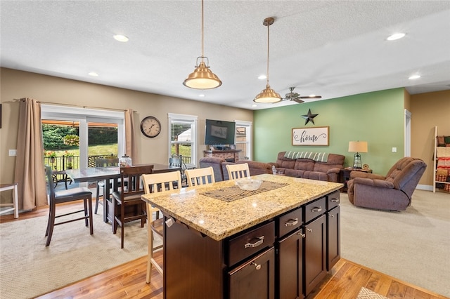 kitchen with ceiling fan, light stone countertops, light colored carpet, decorative light fixtures, and dark brown cabinetry