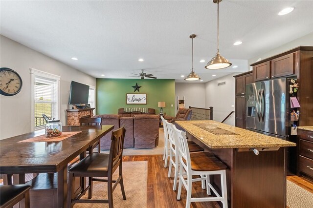 kitchen featuring stainless steel fridge, dark brown cabinets, hanging light fixtures, light wood-type flooring, and ceiling fan