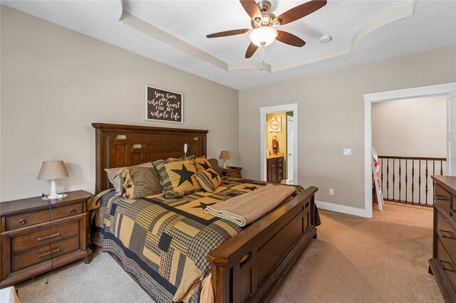 bedroom with light carpet, ensuite bathroom, ceiling fan, and a raised ceiling