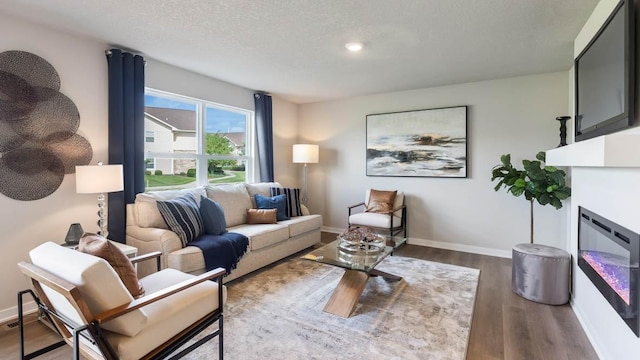living area with baseboards, a textured ceiling, and wood finished floors
