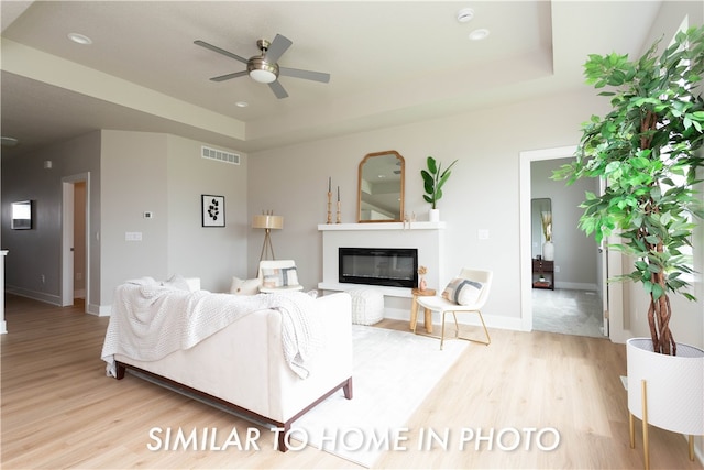 living room featuring light hardwood / wood-style floors, a tray ceiling, and ceiling fan