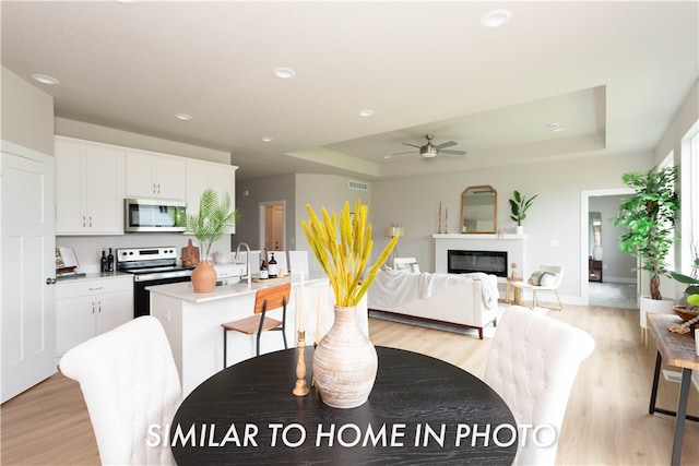 dining space with light hardwood / wood-style floors, ceiling fan, and a raised ceiling