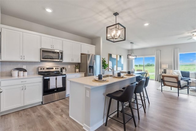 kitchen with appliances with stainless steel finishes, white cabinetry, an island with sink, a kitchen bar, and decorative light fixtures