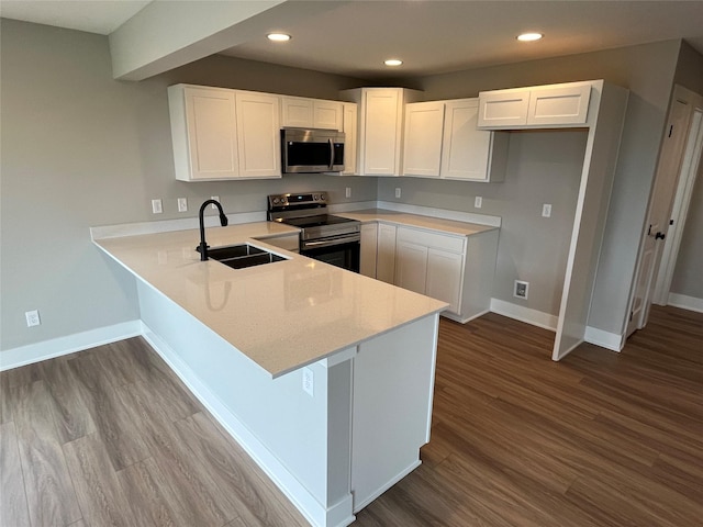 kitchen featuring kitchen peninsula, stainless steel appliances, sink, hardwood / wood-style floors, and white cabinetry