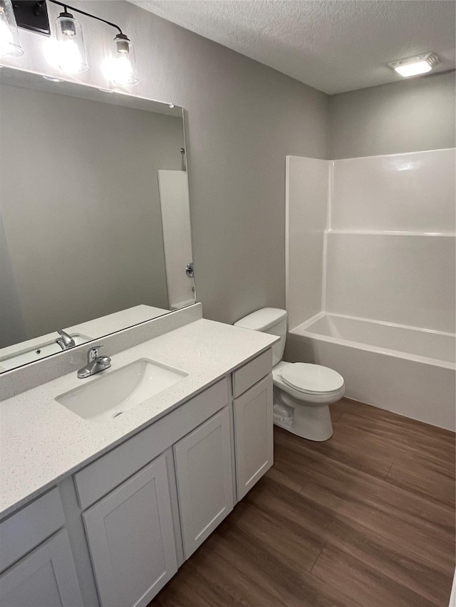 full bathroom with vanity, washtub / shower combination, hardwood / wood-style flooring, toilet, and a textured ceiling