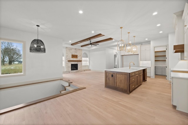 kitchen featuring decorative light fixtures, a kitchen island with sink, ceiling fan, a brick fireplace, and light wood-type flooring