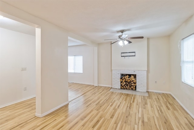 unfurnished living room featuring light hardwood / wood-style flooring, a fireplace, ceiling fan, and a healthy amount of sunlight