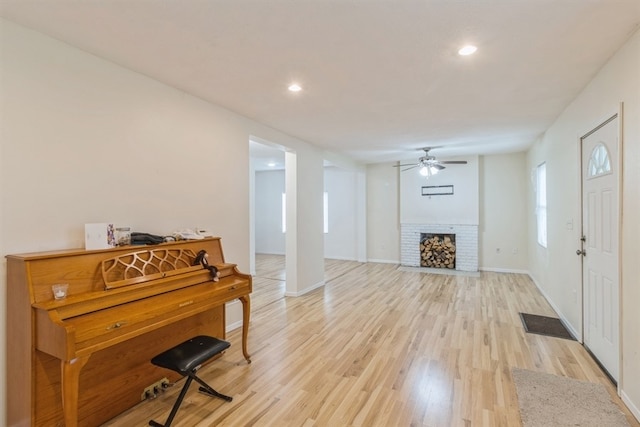 interior space with ceiling fan, light wood-type flooring, and a brick fireplace