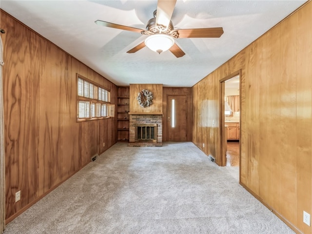 unfurnished living room featuring a textured ceiling, ceiling fan, wooden walls, light carpet, and a fireplace