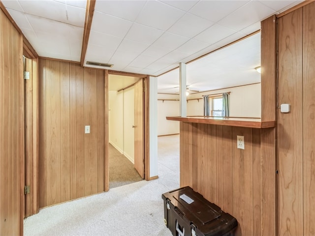 interior space with ceiling fan, wooden walls, and light colored carpet