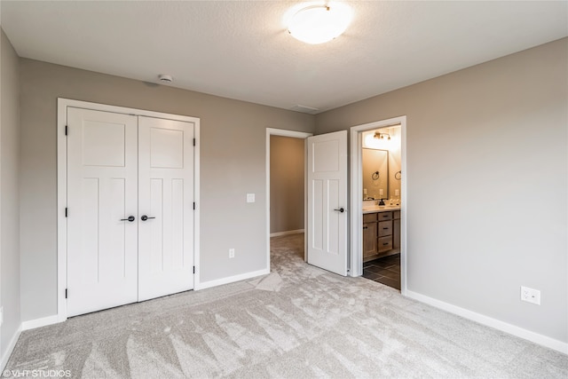 unfurnished bedroom with light colored carpet, a closet, and ensuite bath