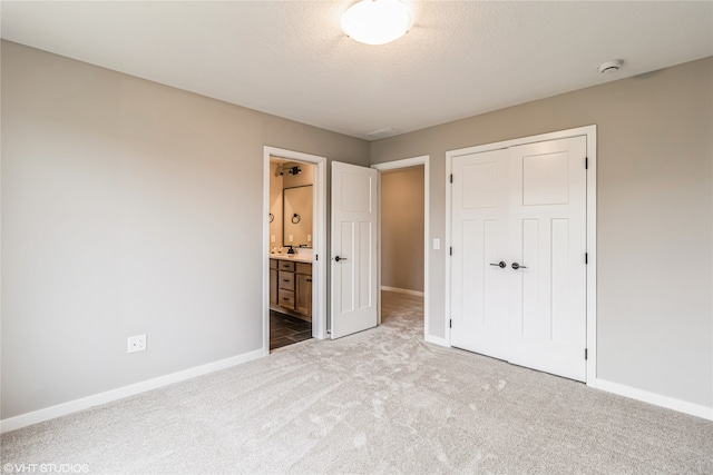 unfurnished bedroom featuring connected bathroom, a closet, a textured ceiling, and carpet flooring