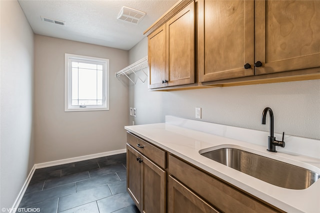 laundry room featuring a textured ceiling, dark tile patterned floors, cabinets, sink, and hookup for a washing machine