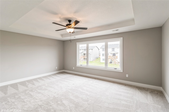 carpeted empty room featuring ceiling fan and a raised ceiling