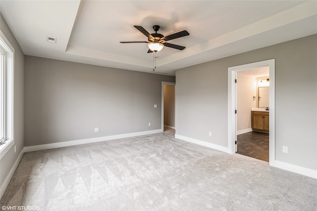 unfurnished bedroom with ceiling fan, ensuite bathroom, carpet floors, and a raised ceiling