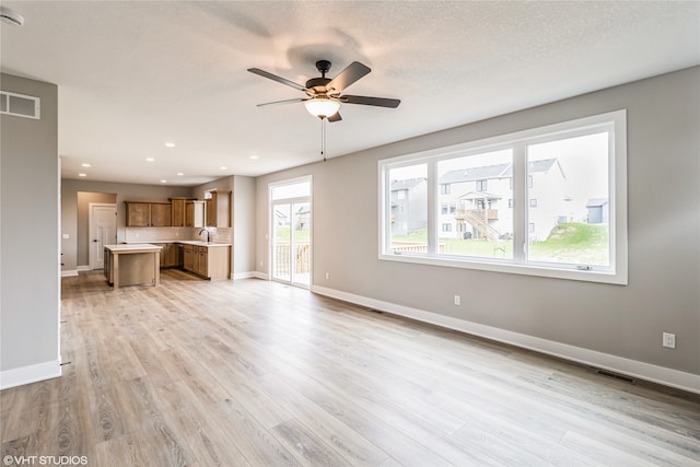 unfurnished living room with ceiling fan, sink, a textured ceiling, and light hardwood / wood-style flooring