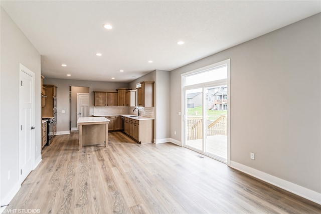 kitchen with backsplash, a kitchen island, a kitchen bar, sink, and light hardwood / wood-style flooring