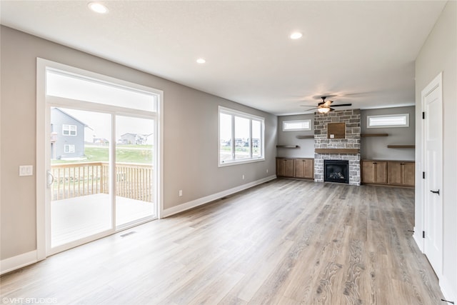 unfurnished living room featuring ceiling fan, light hardwood / wood-style flooring, and a stone fireplace